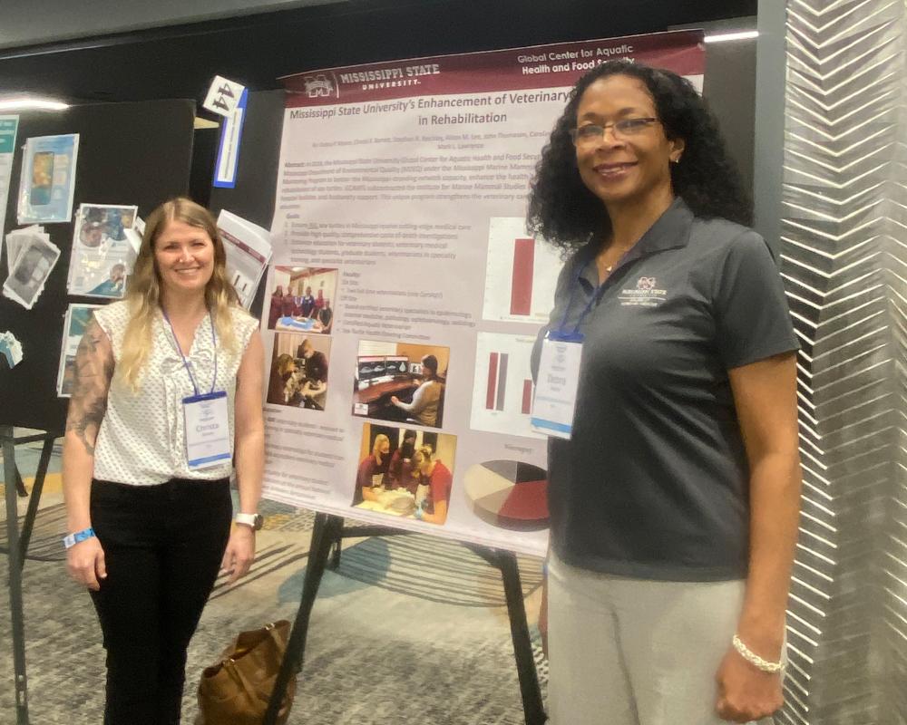 Barrett (left) and Moore (right) are standing next to a GCAHFS poster telling about the program's activities.